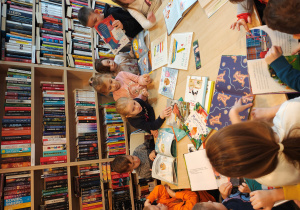 Przedszkolaki siedzą przy stole i oglądają różne książki literatury dziecięcej.