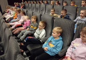 Dzieci siedzą w fotelach sali kinowej.