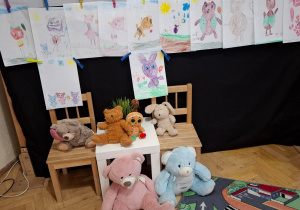 Przypięte do sznurków rysunki misiów. Stolik, krzesła, pluszowe misie.