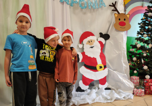 Trzech chłopców w czapkach Mikołaja stoją na tle dekoracji Laponii.