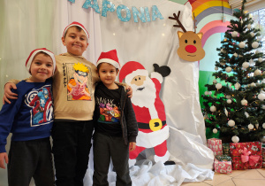 Trzech chłopców w czapkach Mikołaja stoi na tle dekoracji Laponii.