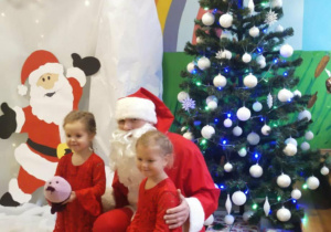 Dwie dziewczynki z Mikołajem pozują na tle dekoracji - Laponii.