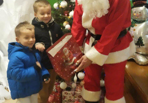 Dwóch chłopców stoi obok Mikołaja z torbą prezentową.