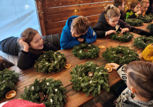 Przedszkolaki siedzą przy stole, na którym leżą wieńce z choinek.