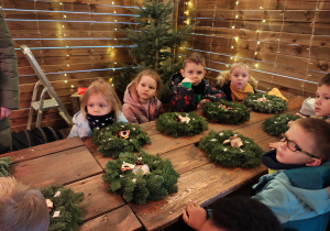Przedszkolaki siedzą przy stole, na którym leżą wieńce z choinek.