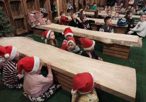 Przedszkolaki siedzą na poduszach przy drewnianych stołach.