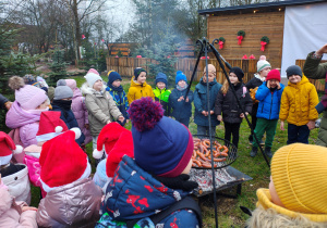Przedszkolaki stoją przy palenisku z kiełbaskami.