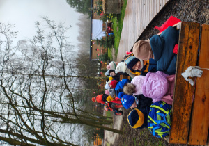 Przedszkolaki siedzą w wagonikach ciągnietych przez mały traktor.