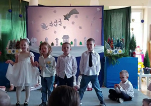 Dziewczynka i trzech chłopców stoi na dywanie. W tle świąteczna dekoracja.