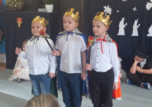 Trzech chłopców w przebraniach trzech króli stoi na dywanie.