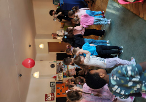 Jeden mężczyzna gra na trąbce, drugi trzyma mikrofon. Dzieci stoją przed nimi na dywanie.