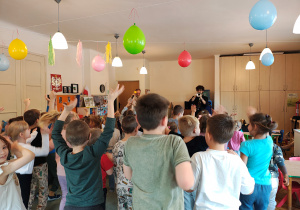 Jeden mężczyzna gra na trąbce, drugi trzyma mikrofon. Dzieci stoją przed nimi na dywanie.