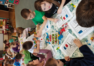 Przedszkolaki wyklejają flagę Francji bibułą oraz kolorują obrazek pastelami.