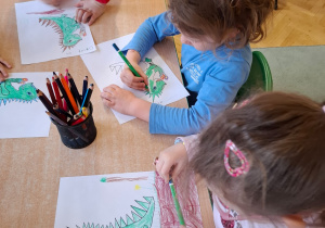 Przedszkolaki kolorują obrazki smoków.
