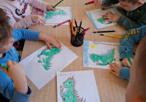 Przedszkolaki kolorują obrazki smoków.