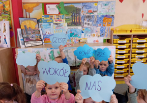 Przedszkolaki trzymają napis "Czyste powietrze wokół nas", w tle obrazki dymów.