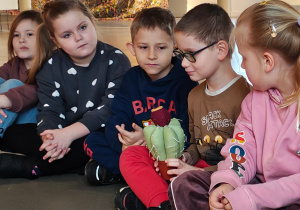 Dzieci siedzą na podłodze w kole. Chłopiec trzyma pluszową opuncję figową.