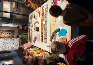 Dzieci stoją przy stole, na którym leżą rózne materiały w etniczne wzory.