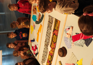 Dzieci stoją przy stole, na którym leżą rózne materiały w etniczne wzory.