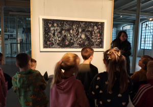 Przedszkolaki stoją przed obrazem. Obok obrazu stoi kobieta.