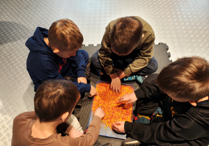 Przedszkolaki siedzą rysując po czerwono-pomarańczowym ryżu.