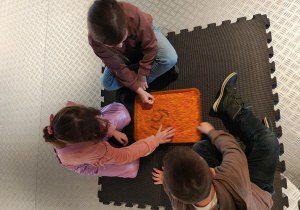 Przedszkolaki siedzą rysując po czerwono-pomarańczowym ryżu.