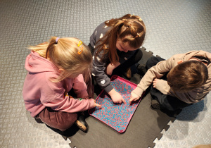 Przedszkolaki siedzą rysując po niebiesko-różowym ryżu.