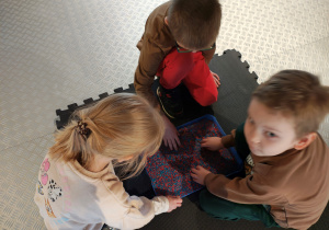 Przedszkolaki siedzą rysując po niebiesko-różowym ryżu.