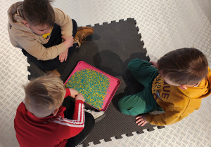 Przedszkolaki siedzą rysując po niebiesko-żółtym ryżu.