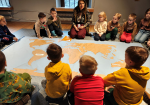 Kobieta wraz z dziećmi siedzi dookoła materiałowej mapy świata.