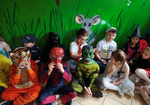 Przebrane za bohaterów bajek oraz inne postacie przedszkolaki siedzą na podłodze.