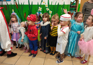 Przebrane za bohaterów bajek oraz inne postacie przedszkolaki stoją w korytarzu.