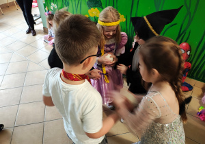 Pięcioro dzieci stoi w kole. Jedna z dziewczynek trzyma piłkę.