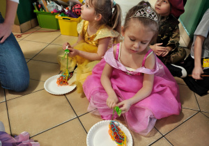 Dwie dziewczynki siedzą na podłodze i nawijają zieloną włóczkę na widelec. W tle przedszkolaki siedzace na podłodze.