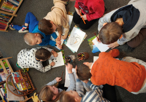 Przedszkolaki leżą na dywanie i kolorują smoki.