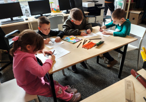 Przedszkolaki siedzą przy stole i kolorują smoki.