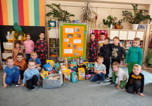 Przedzkolaki pozujące do zdjęcia z plakatem zbiórki dla zwierząt i przyniesionymi darami dla Łódzkiego Towarzystwa Opieki nad Zwierzętami.