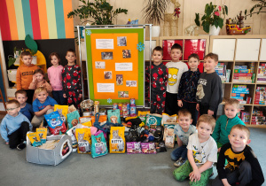Przedzkolaki pozujące do zdjęcia z plakatem zbiórki dla zwierząt i przyniesionymi darami dla Łódzkiego Towarzystwa Opieki nad Zwierzętami.