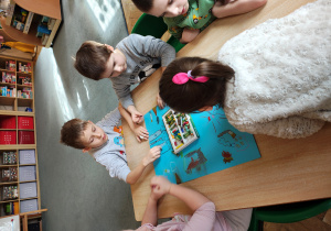 Przedszkolaki siedzą przy stole i malują pastelami na niebieskim kartonie.