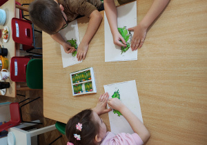Przedszkolaki siedzą przy stole i kolorują smoka.