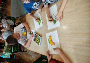 Przedszkolaki siedzą przy stole i kolorują smoka.